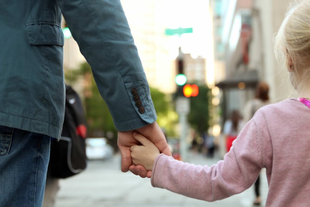 father holding the daughter/ child hand behind the traffic lights